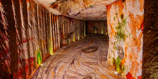 Photographie de la scénographie lumineuse dans les Caves Monmousseau. Projection lumineuse d'œuvres représentant les Châteaux de la Loire sur les murs de la carrière de tuffeau