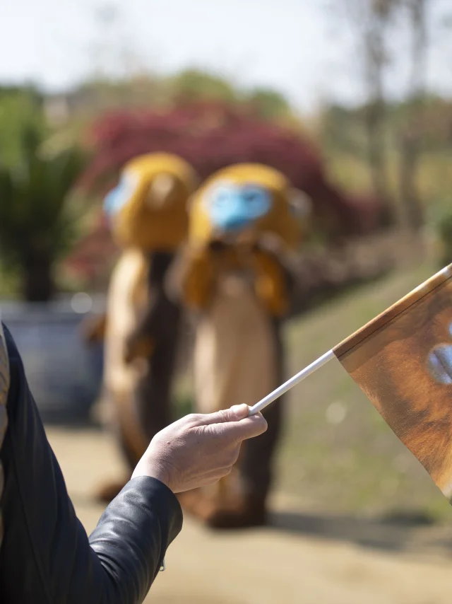 Femme souriante tenant un drapeau du ZooParc de Beauval entourée de deux mascottes de singes dorés.